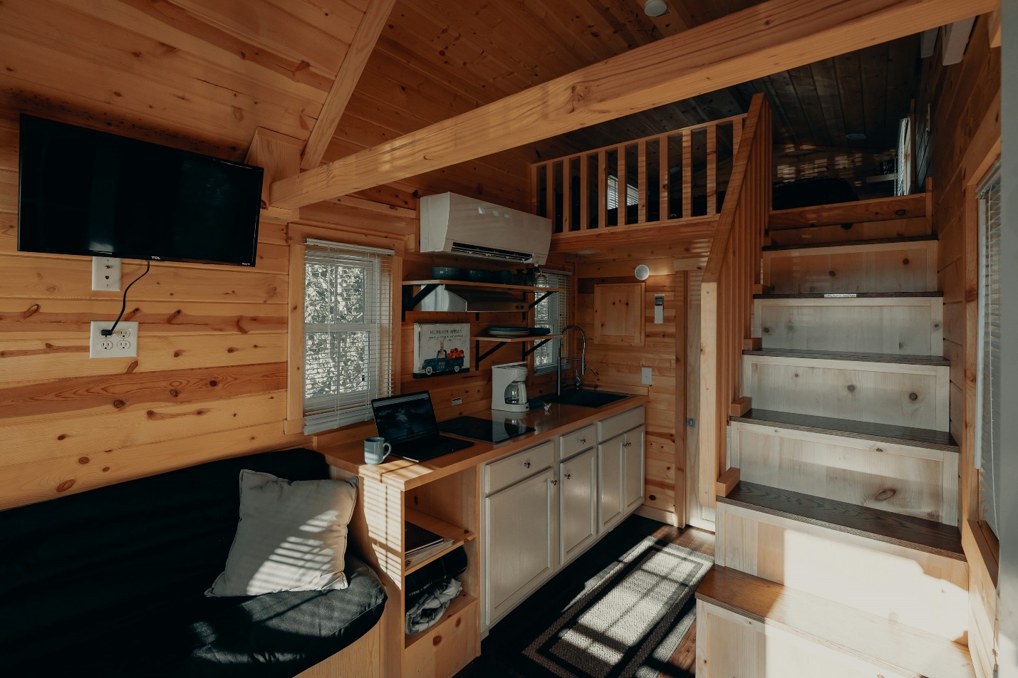 An interior of a small home with a kitchen, stairs, and living room with an AC
