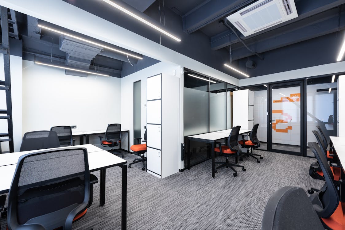 An office with tables and chairs and HVAC work on the ceiling