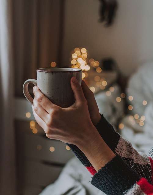 A person holding a warm mug of coffee or tea in front of a cozy window.